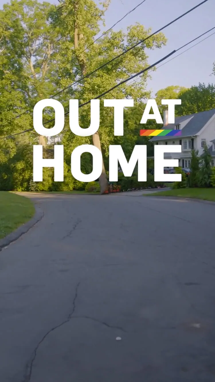 Out at Home text with a rainbow flag overlay on a suburban street.