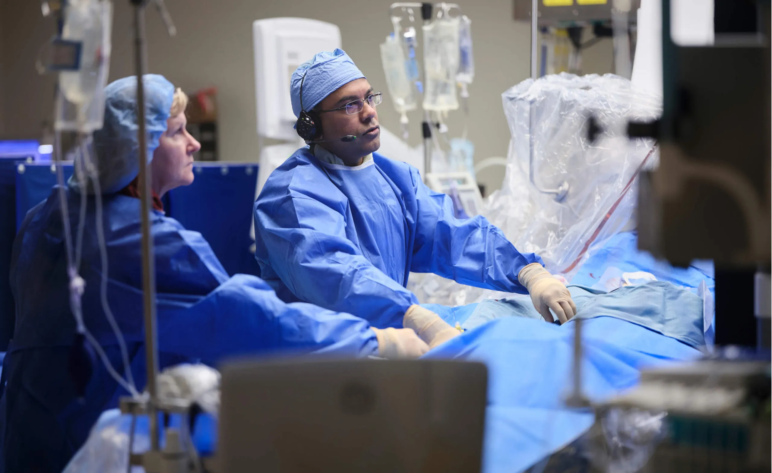 Two surgeons in blue scrubs and caps perform a medical procedure in an operating room.