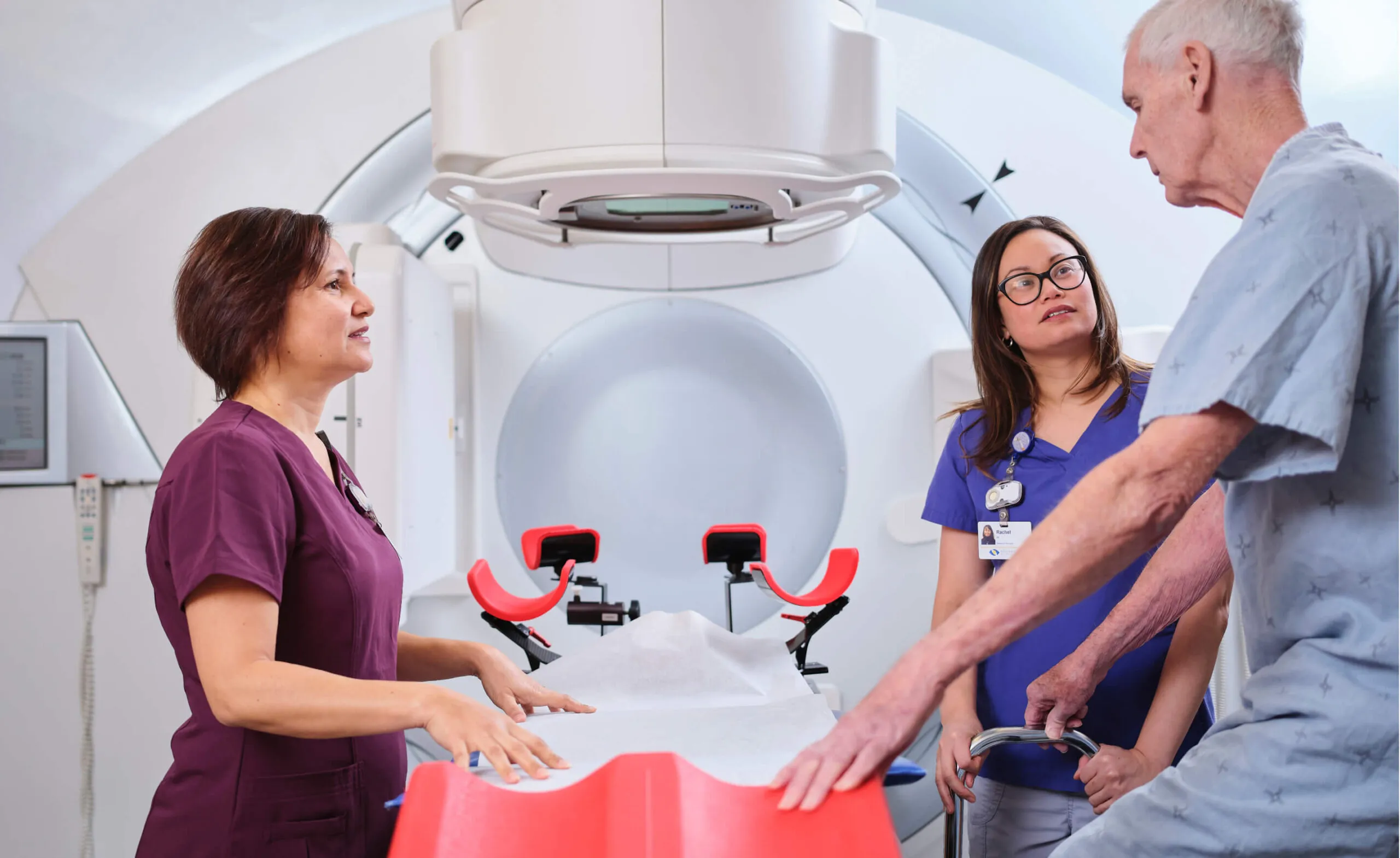 Medical staff assist an elderly patient near a radiation therapy machine.