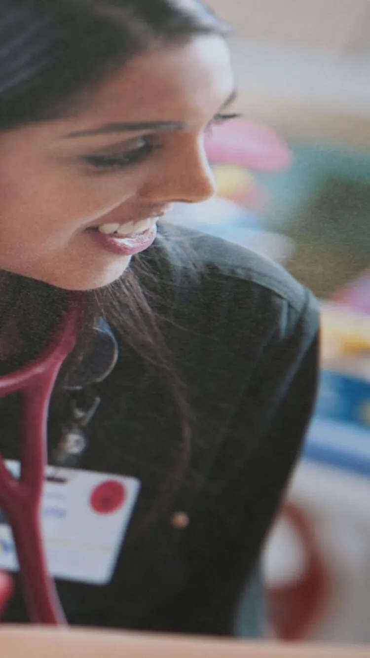A nurse smiles while wearing a stethoscope and ID badge.