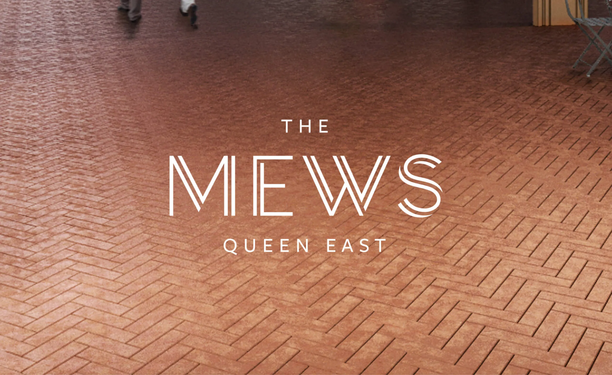 The Mews Queen East logo on a brick patterned background.