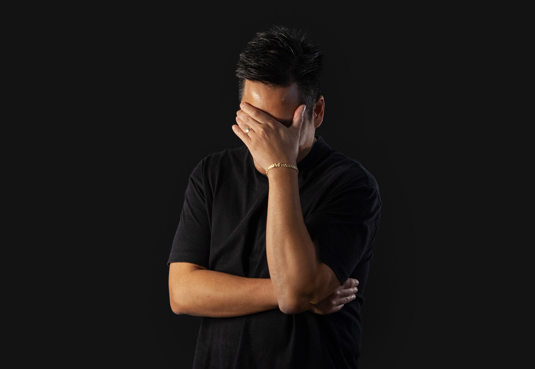 Man in black shirt covering face with hand.