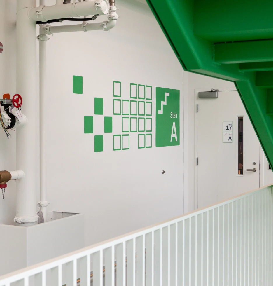 Green stairwell signage with abstract green squares on a white wall.