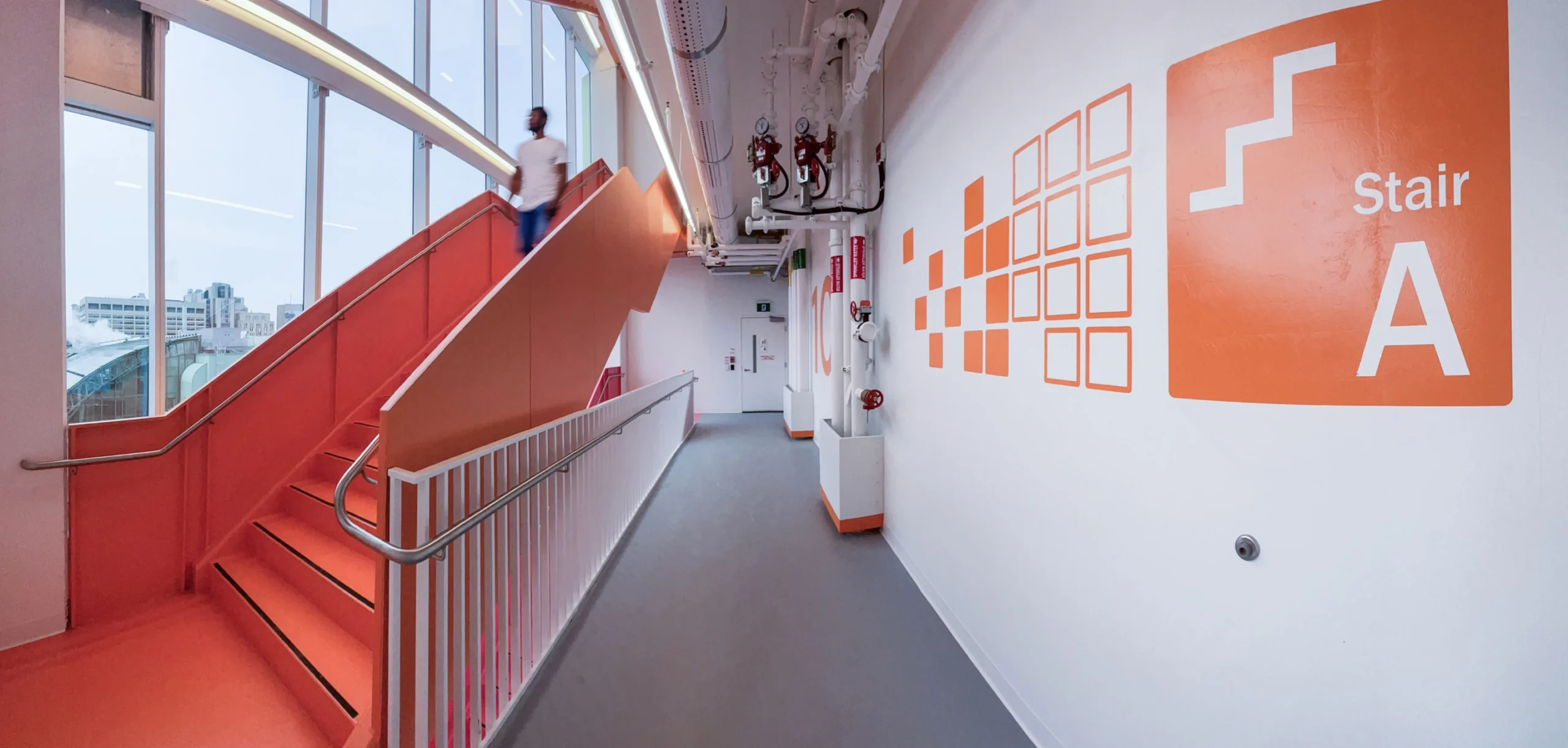 Modern orange staircase with a person walking down, leading to a hallway with 