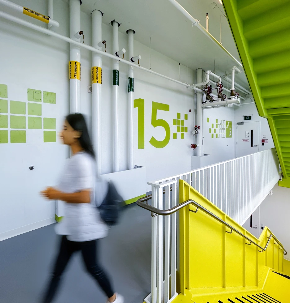 Modern hallway with bright yellow stairs and green accents, a person walks by.