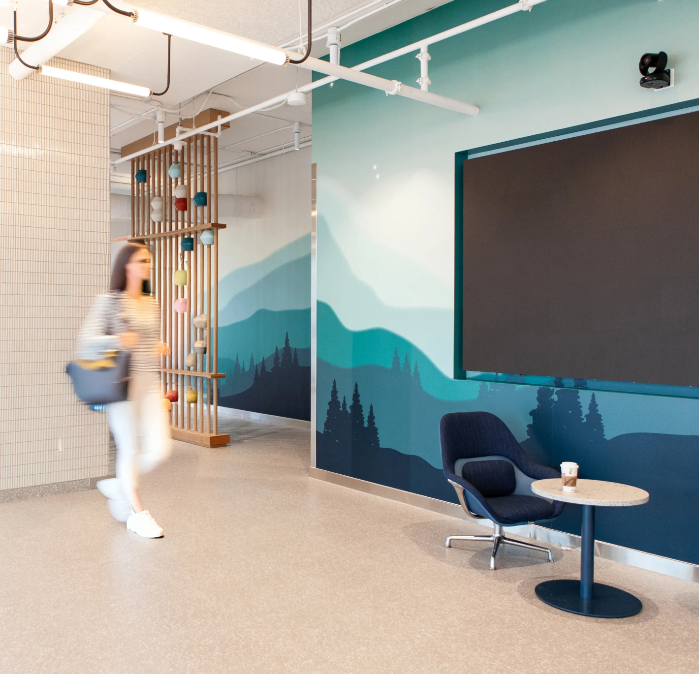 Modern office interior with a woman walking past a decorative screen and a mural.
