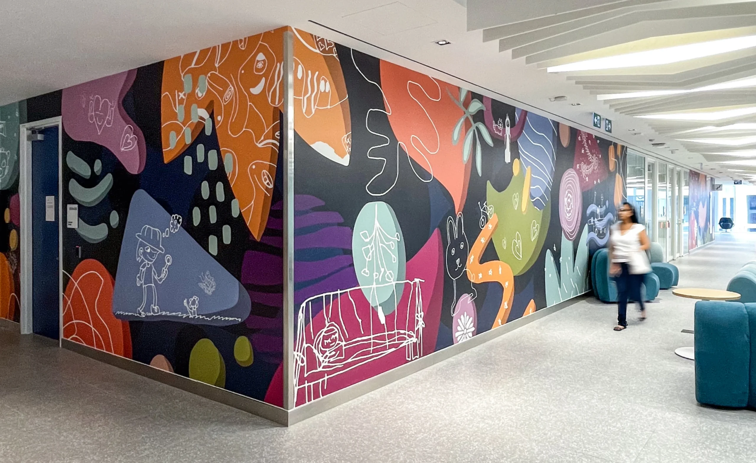 A colourful mural with abstract shapes and cartoon drawings adorns a hallway with teal seating.