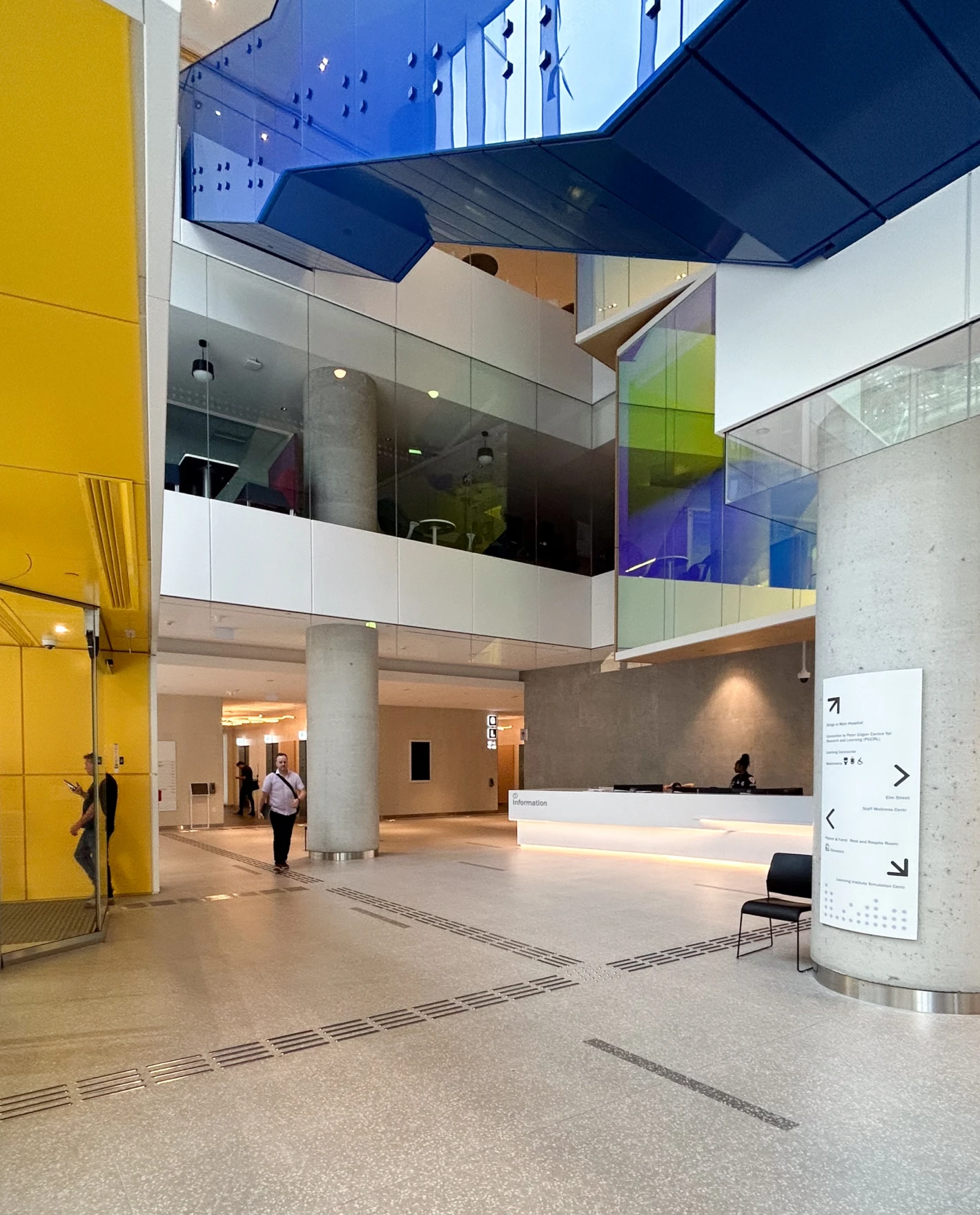 Modern hospital lobby with yellow and blue accents, a reception desk, and people walking.