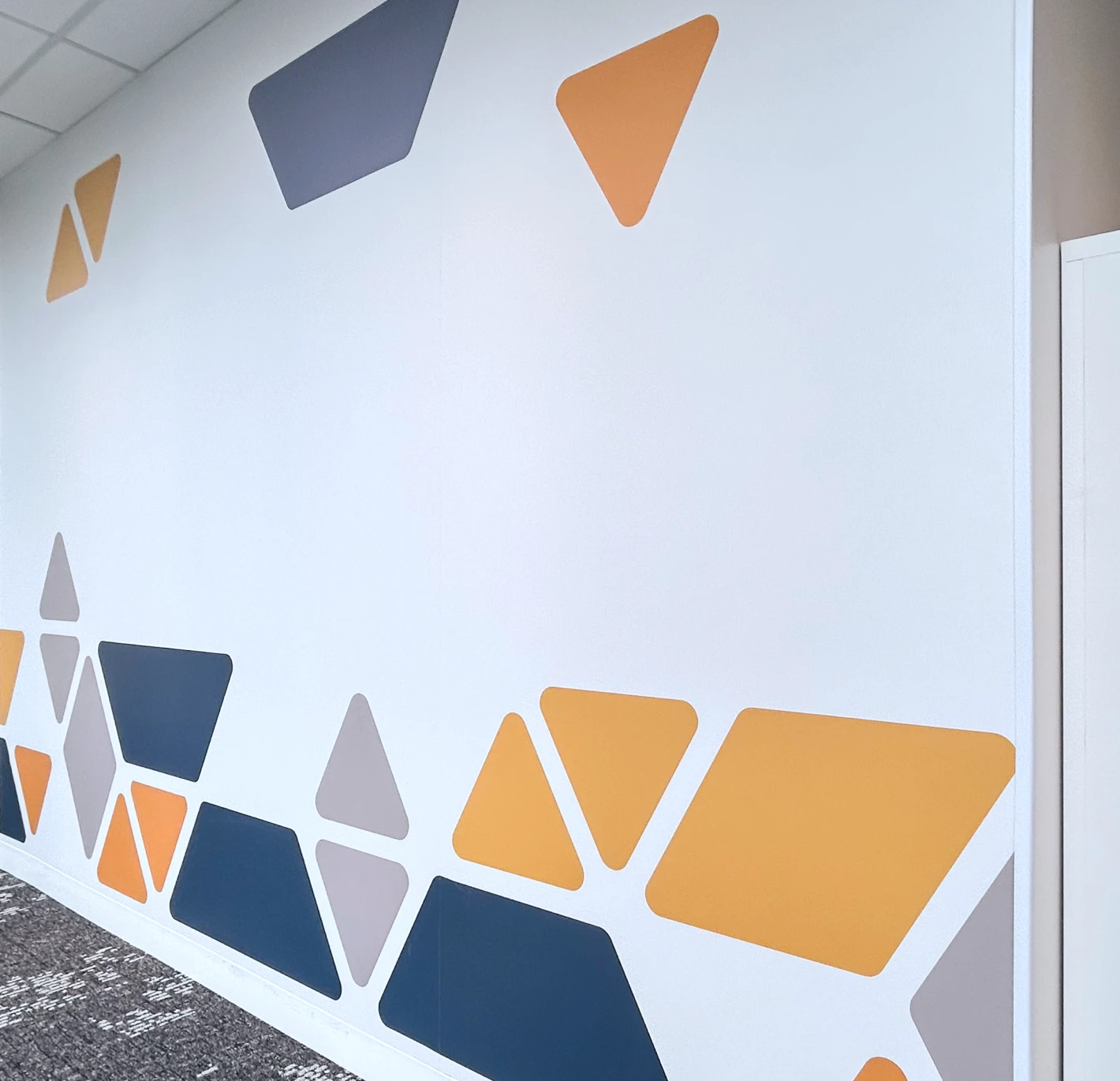 Abstract geometric pattern on a white wall with orange, grey and blue shapes.
