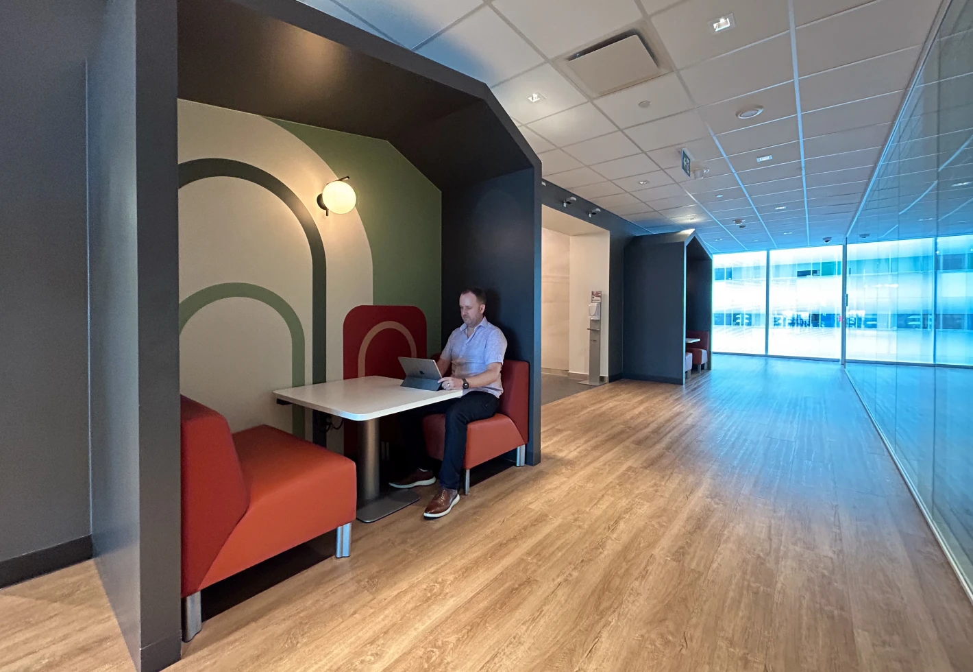 Man working on a laptop in a modern office booth with orange seating and a geometric mural.