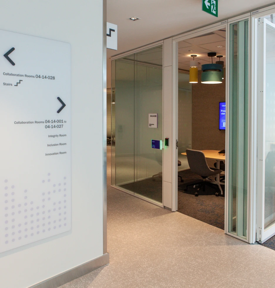 Modern office hallway with glass-walled meeting rooms and directional signage.